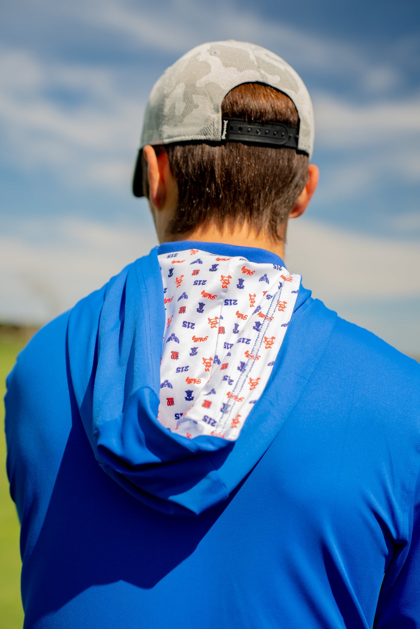 Back view of blue golf hoodie with hood down, showing interior lining covered in red and blue Philly sports-inspired icons for added personality.
