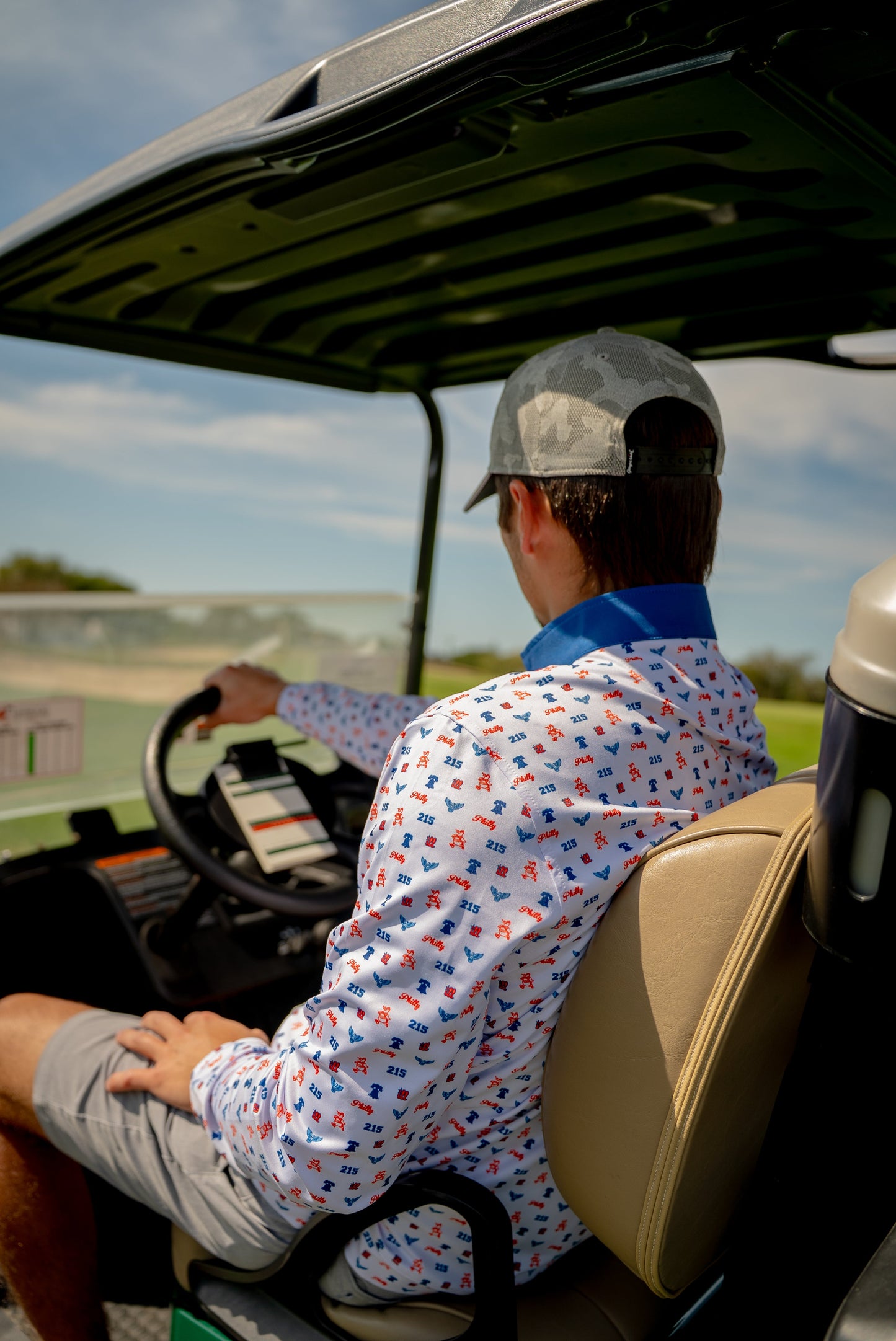 Lifestyle shot of The Phrenetic Zip worn in a golf cart, back and side view—Philly attitude meets fairway comfort in this bold men's quarter zip.